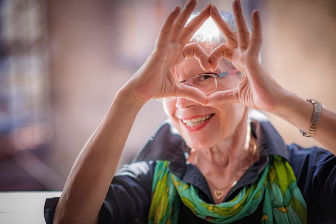 A senior woman making a heart with her fingers.