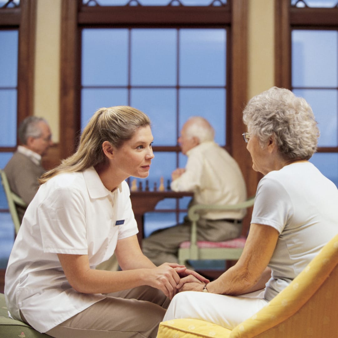 A caregiver sitting with an elderly woman in a senior living facility
